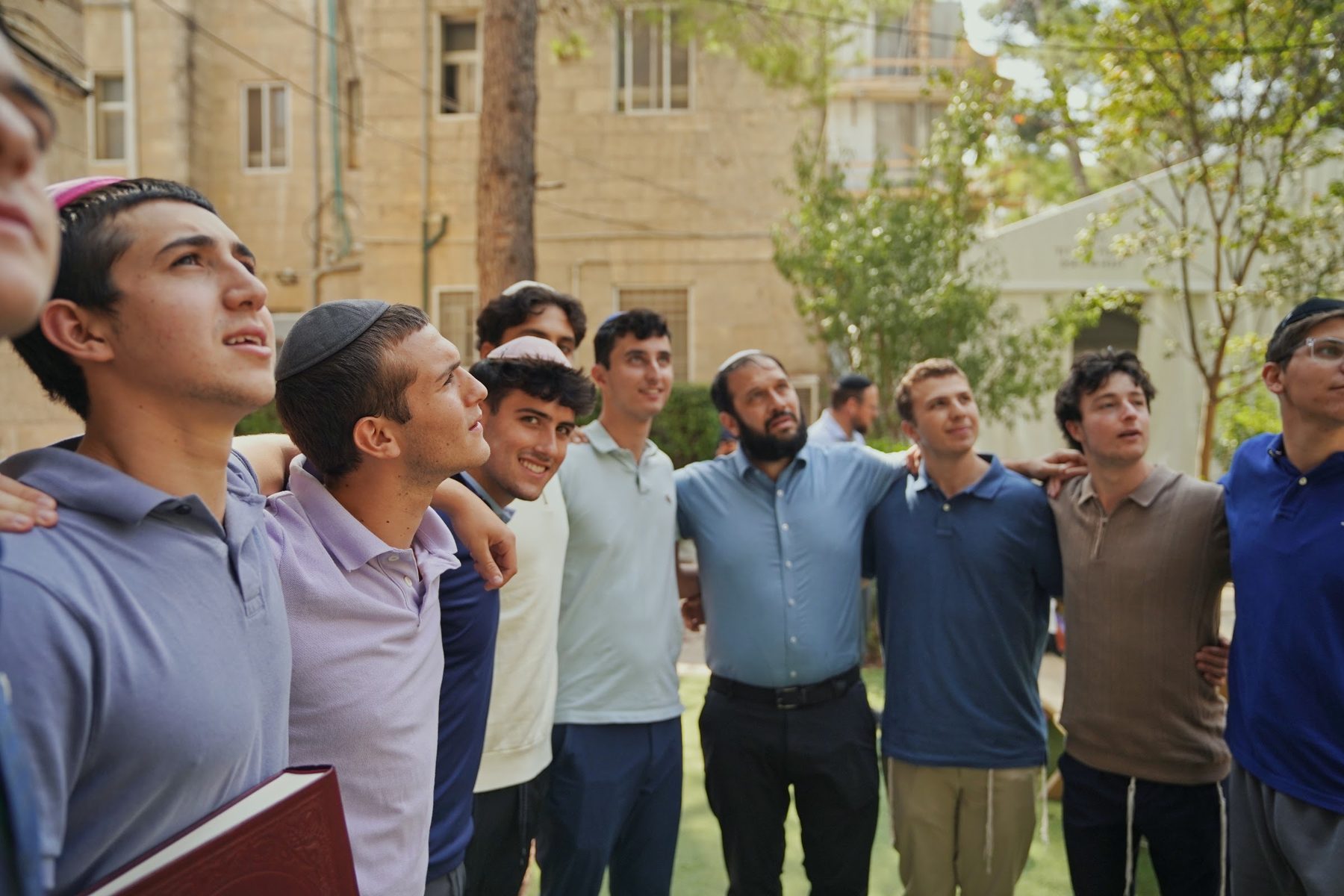 Talmidim and a Rebbe singing, arms around each other, in the campus courtyard