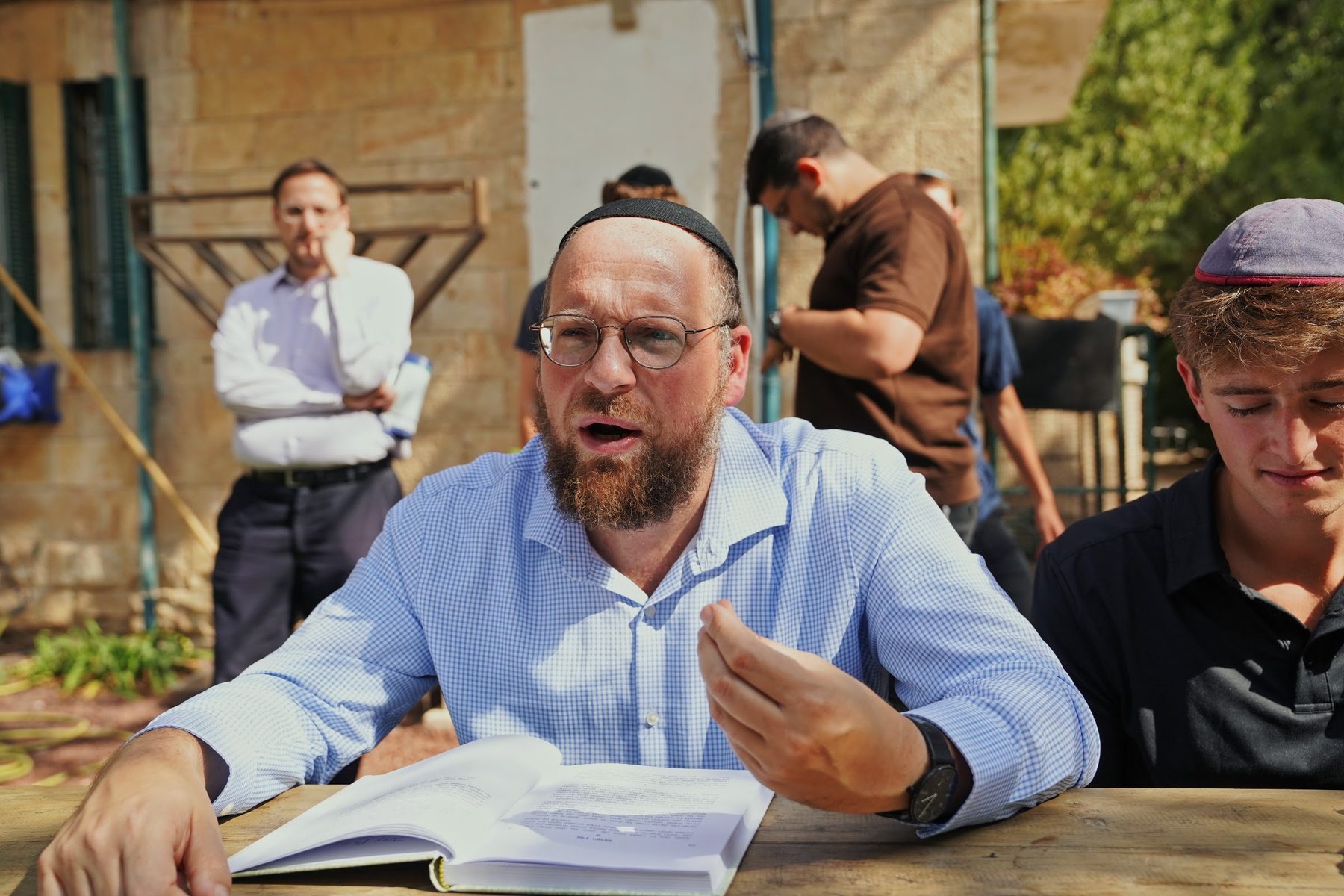 A Rebbe learning with talmidim at a table in the campus garden