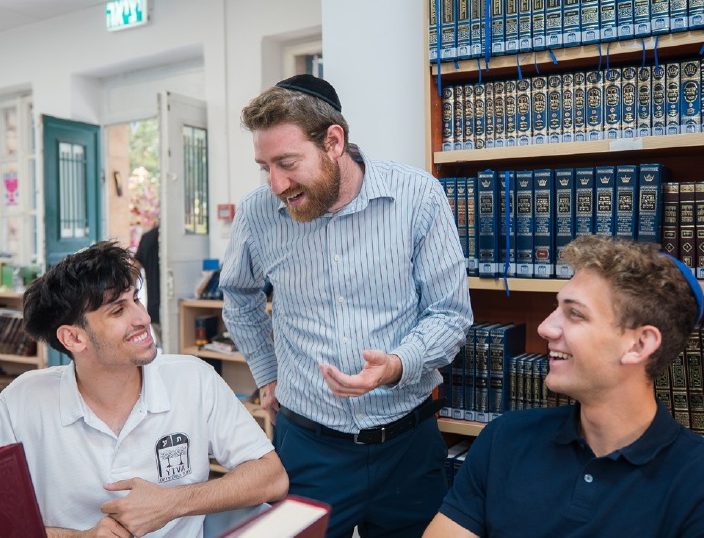A Rebbe with two talmidim by the shelves of sefarim, all three laughing