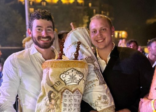 Two talmidim holding a Sefer Torah at a night celebration